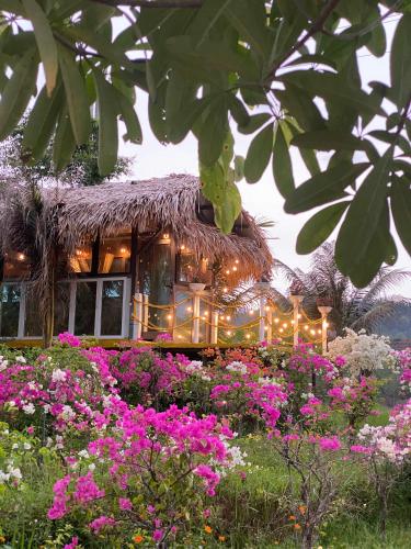 a building with a thatch roof and a field of flowers at Mai Chau Onsen Retreat in Mai Chau