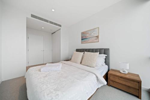 a white bedroom with a large bed and a wooden table at Luxury Perth CBD Apartment with Pool & Gym - Sleeps 3 in Perth