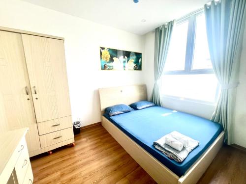 a bedroom with a bed with blue sheets and a window at IMPERIAL PLACE - NATURAL POEM View đẹp - hồ bơi, gym miễn phí in Ho Chi Minh City