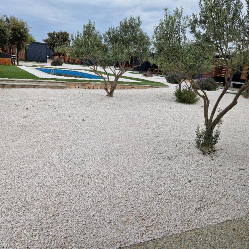 a gravel yard with two trees and a swimming pool at Mobile Homes Albatross Pirovac in Pirovac