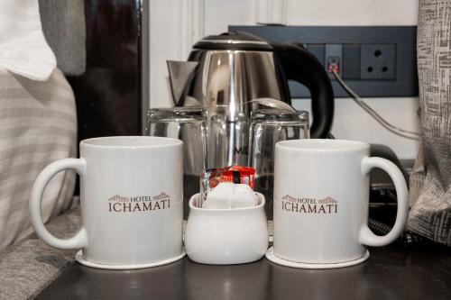 three coffee mugs sitting on a counter with a coffee pot at Hotel Ichamati in Kolkata