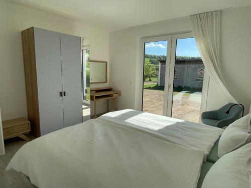 Dormitorio blanco con cama y puerta corredera de cristal en Ferienresort Weidelbach, en Spangenberg