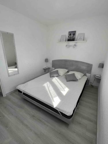 Cette chambre comprend un grand lit avec des draps blancs et un miroir. dans l'établissement maison 4 personnes avec piscine, mer 200m à pieds, à Marseillan