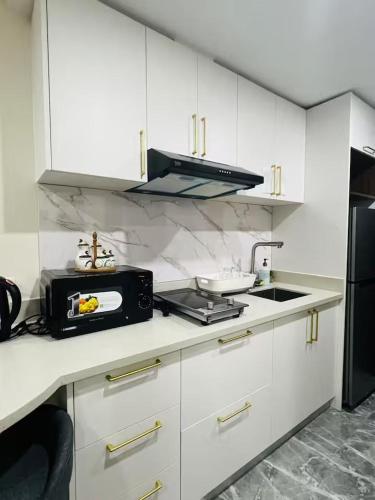 a kitchen with white cabinets and a sink and a microwave at Baguio Condo - City Hub - Urban Oasis in Pines with Pool & Mountain View in Baguio