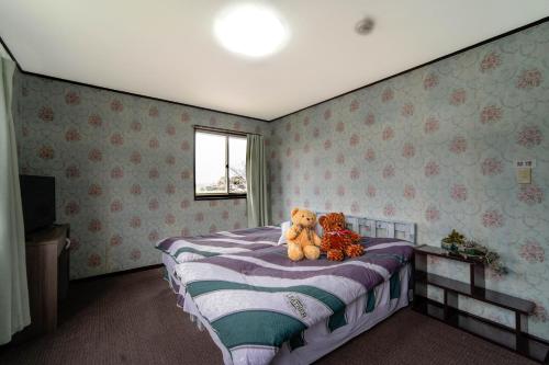 two teddy bears sitting on a bed in a bedroom at 竹の荘 in Nasukarasuyama