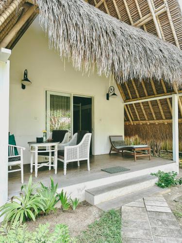 a patio with chairs and a table and a straw roof at Vayam Boutique Resort Gili Asahan in Gili Asahan