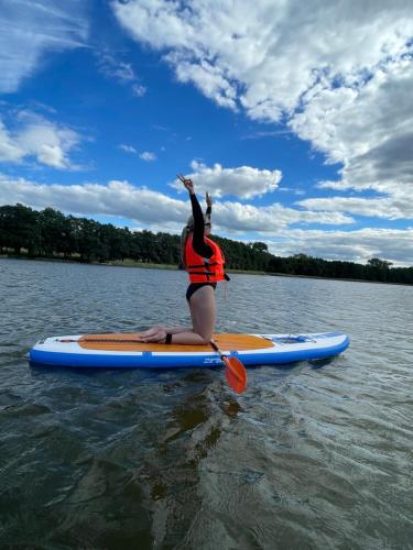 a woman sitting on a paddle board in the water at MIĘDZY NAMI domki nad jeziorem in Kołczewo