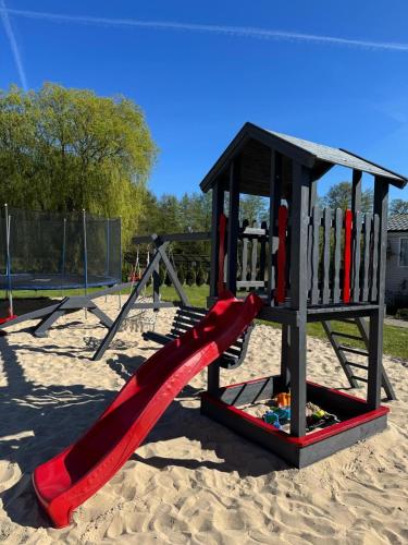 a playground with a red slide in the sand at MIĘDZY NAMI domki nad jeziorem in Kołczewo