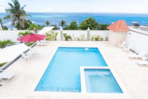a swimming pool with chairs and an umbrella and the ocean at Gaviota Paradise in La Romana