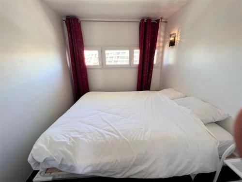 - une petite chambre avec un lit blanc et des rideaux rouges dans l'établissement VILLAGE NATURISTE - CAP d'AGDE - PORT NATURE 2 - VUE MER - COURSIVE, au Cap d'Agde