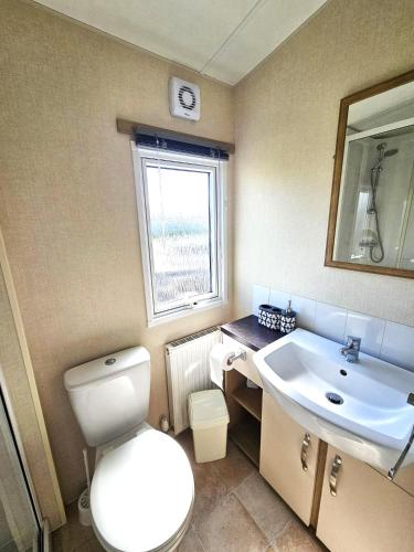 a bathroom with a toilet and a sink and a window at Northcott 68, Bude in Poughill