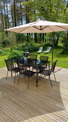 une table et des chaises sous un parasol sur une terrasse dans l'établissement La maison au cœur de la forêt, à Rosporden
