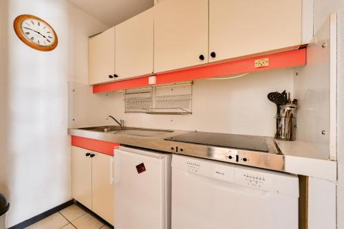 une cuisine avec des placards blancs et une horloge murale dans l'établissement Résidence Le Tourmalet - maeva Home - Appartement 3 pièces 8 personnes - Sélection MAE-0511, à La Mongie