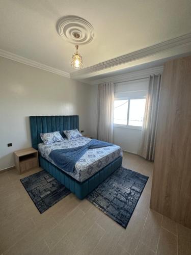 a bedroom with a bed with a blue headboard and a window at Appartement à Houma, proche Port Tanger Med in Dalia
