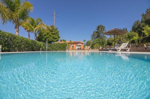 a large blue swimming pool with an umbrella and chairs at Quinta Gomes in Lagos