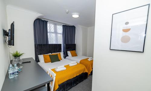 two beds in a room with a table and a desk at Woodford Hotel in London