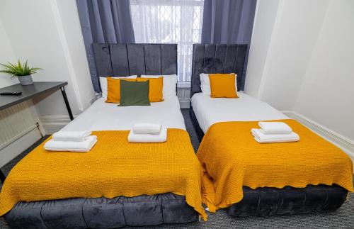 two beds in a room with orange and green pillows at Woodford Hotel in London