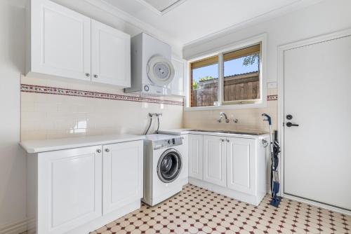 a kitchen with white cabinets and a washer and dryer at Spacious Family Home with Balcony in Pascoe Vale in Melbourne