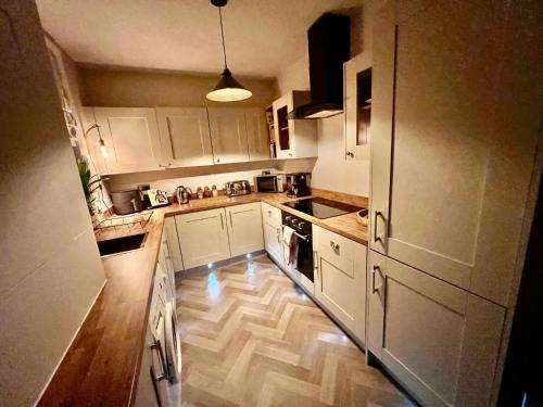 a kitchen with white cabinets and a wooden floor at Olive Tree Cottage in Golcar