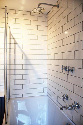 a white tiled bathroom with a bath tub at Lovely cottage with private garden in Penryn