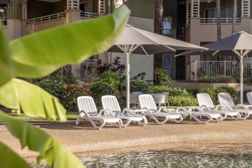 a row of white chairs and umbrellas next to a pool at Mantra Amphora in Palm Cove