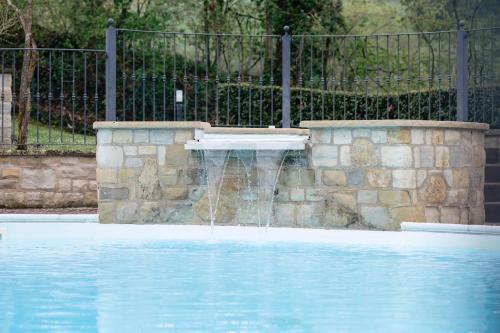 a swimming pool with a fountain in front of a fence at Le Fontanelle Country House in SantʼIppolito