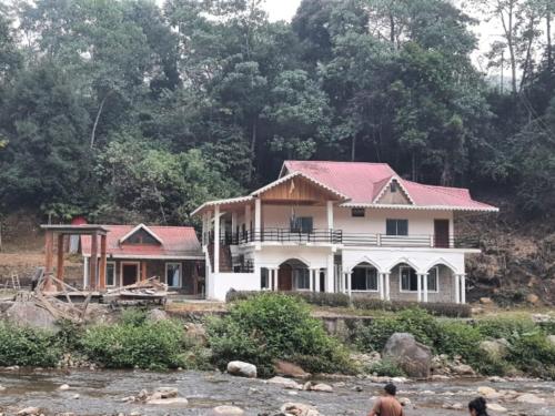 a house with a red roof next to a river at Aranyak Homestay By StayApart in Simāna Basti
