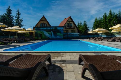 a swimming pool with chairs and umbrellas in front of a house at Highland in Yablunytsya