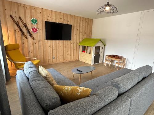 un salon avec un canapé gris et une télévision dans l'établissement La Jonquille, Appartement Centre Ville de Gérardmer, linge et ménage inclus, à Gérardmer