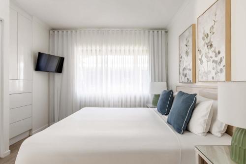 a white bedroom with a large bed with blue pillows at Mantra Amphora in Palm Cove