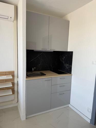 une cuisine avec des armoires blanches et un évier dans l'établissement Studio vue mer avec parking Héliopolis village naturiste, au Cap d'Agde