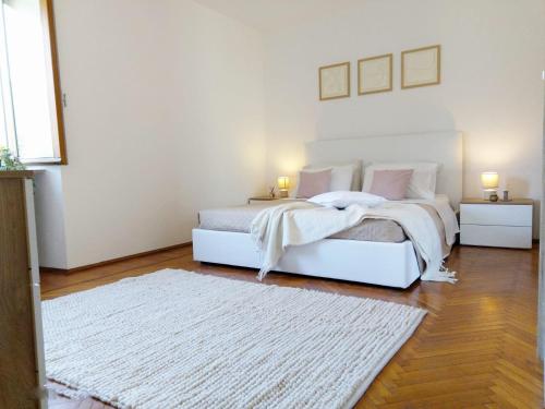 a white bedroom with two beds and a rug at QuickHome Appartamento Gelsomino in Andorno Micca