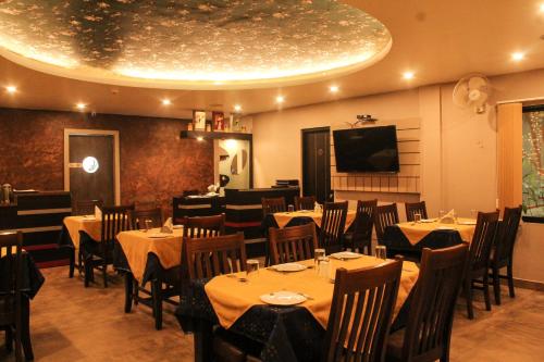 a restaurant with tables and chairs and a flat screen tv at Hotel Rajawas in Dibrugarh
