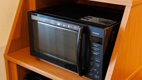 a black microwave oven sitting on a wooden shelf at JR-East Hotel Mets Komagome in Tokyo