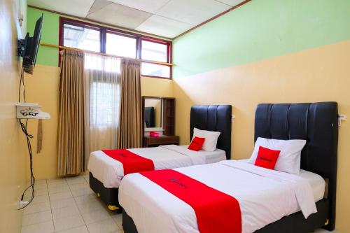 two beds in a hotel room with red and white sheets at RedDoorz Syariah at Omah Pathok Malioboro in Yogyakarta