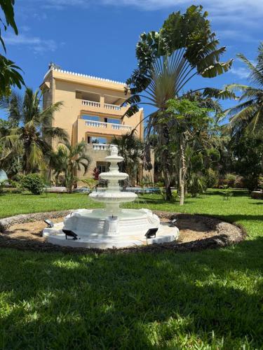 a white fountain in the grass in front of a building at Tamasha Luxury Villa - Diani in Diani Beach