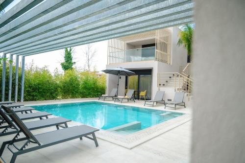 a swimming pool with chairs and an umbrella on a patio at Grand Kourouta Pool Apartments in Kourouta