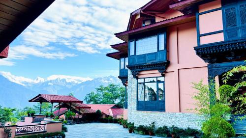 a pink building with windows and mountains in the background at The Chumbi Mountain Retreat & Spa, A Club Mahindra Associate in Pelling
