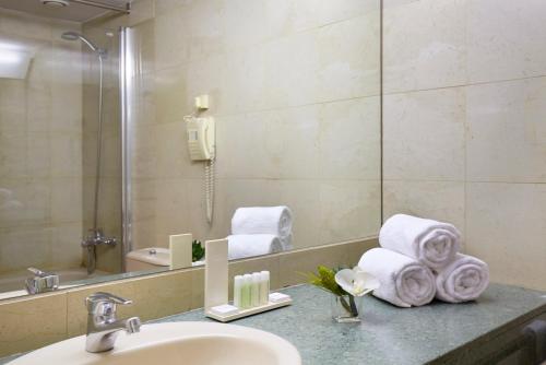 y baño con lavabo, espejo y toallas. en Sercotel Delfos Andorra, en Andorra la Vella