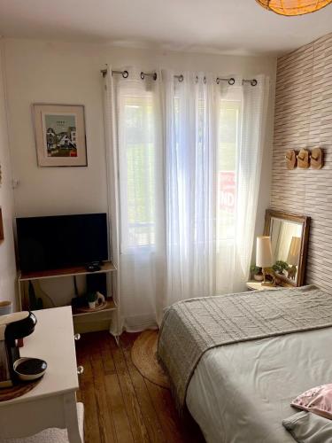 Cette chambre comprend un lit avec des rideaux blancs et une télévision. dans l'établissement Petit cocoon face au Château de Caen, à Caen