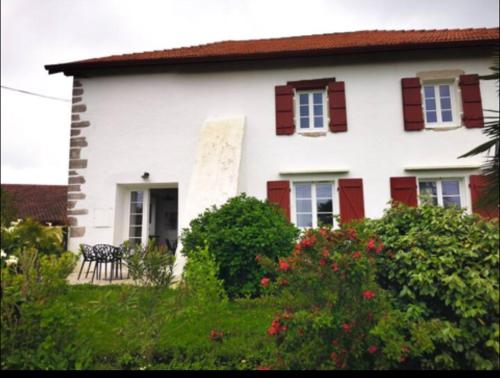 a white house with red shuttered windows and bushes at Duplex 2 chambres avec jardin 15 mn de Bayonne à Urt in Urt