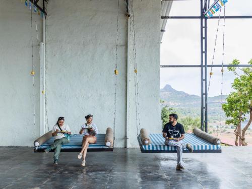 three young men sitting on benches in a room with windows at The Hosteller Bhandardara in Bhandardara 