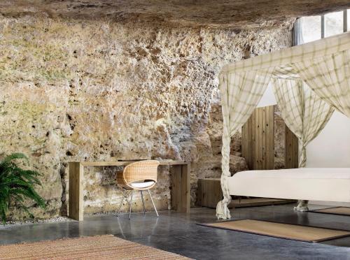 a bedroom with a bed and a chair in front of a stone wall at Cuevas del Pino Turismo Rural y Emocional SL in Villarrubia