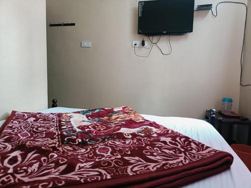 a red blanket on a bed with a tv on the wall at Yamuna Residency by HRS Stays in Ooty