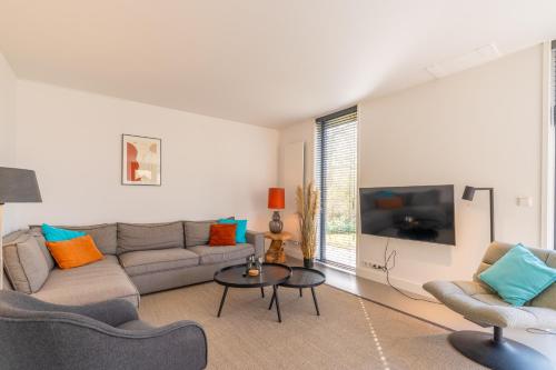 Una sala de estar con un sofá y sillas y un televisor. en De Wadden Parel - Villa 184, en Den Burg