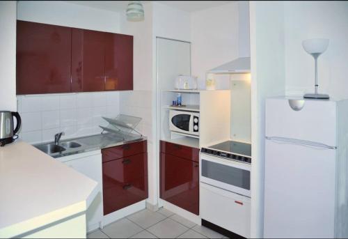 une cuisine avec des armoires rouges et un réfrigérateur blanc dans l'établissement Vaillant Couturier - Lyon 2 - LB Quiet and bright with terrace and private parking, à Vénissieux