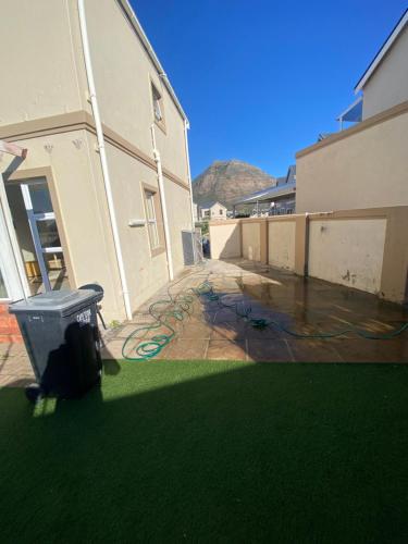 a yard with green grass and a building with a trash can at Cosy Guesthouse near Muizenberg Beach in Muizenberg