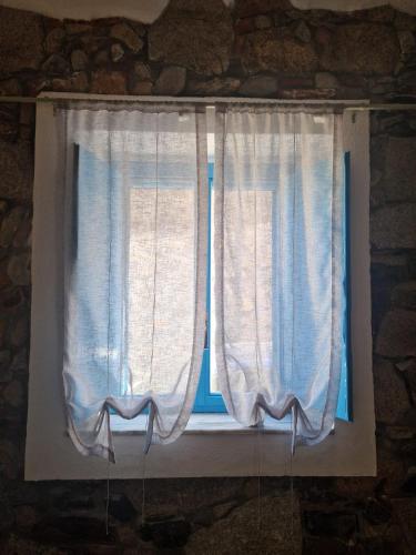 a window with white curtains on a stone wall at Su Furriadroxiu in San Vito