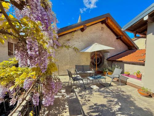 a patio with chairs and an umbrella and a tree with purple flowers at Casbah, suites nel cuore di Menaggio in Menaggio