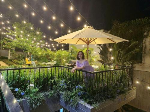 a woman sitting on a balcony under an umbrella at VILLA VENUS -Khu B Không mất vé cổng - tại Khu du lịch sinh thái Đại Lải in Thanh Cao